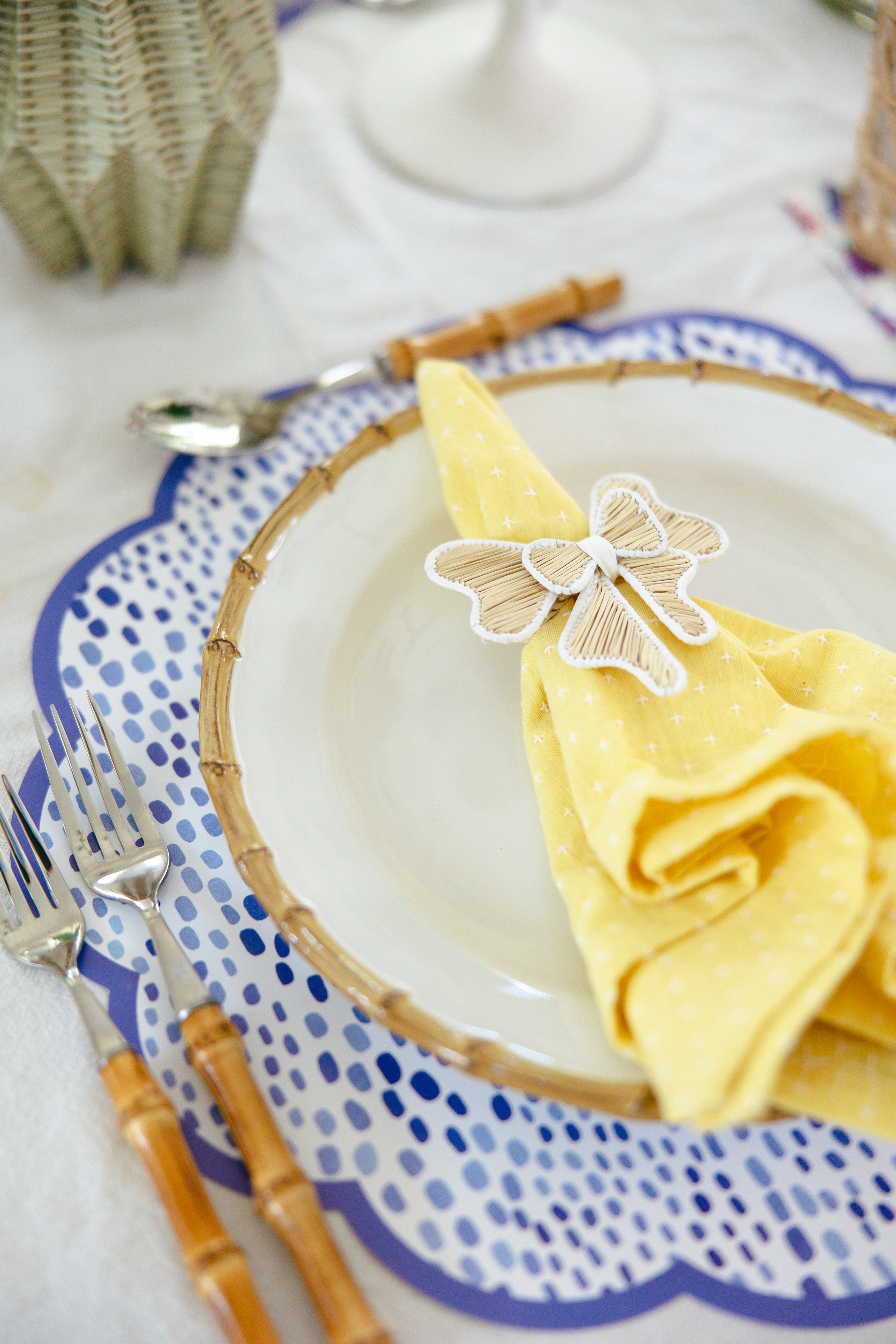 Close up shot of one place setting with purple ikat placemat, yellow napkin in a bow napkin ring and bamboo flatware.
