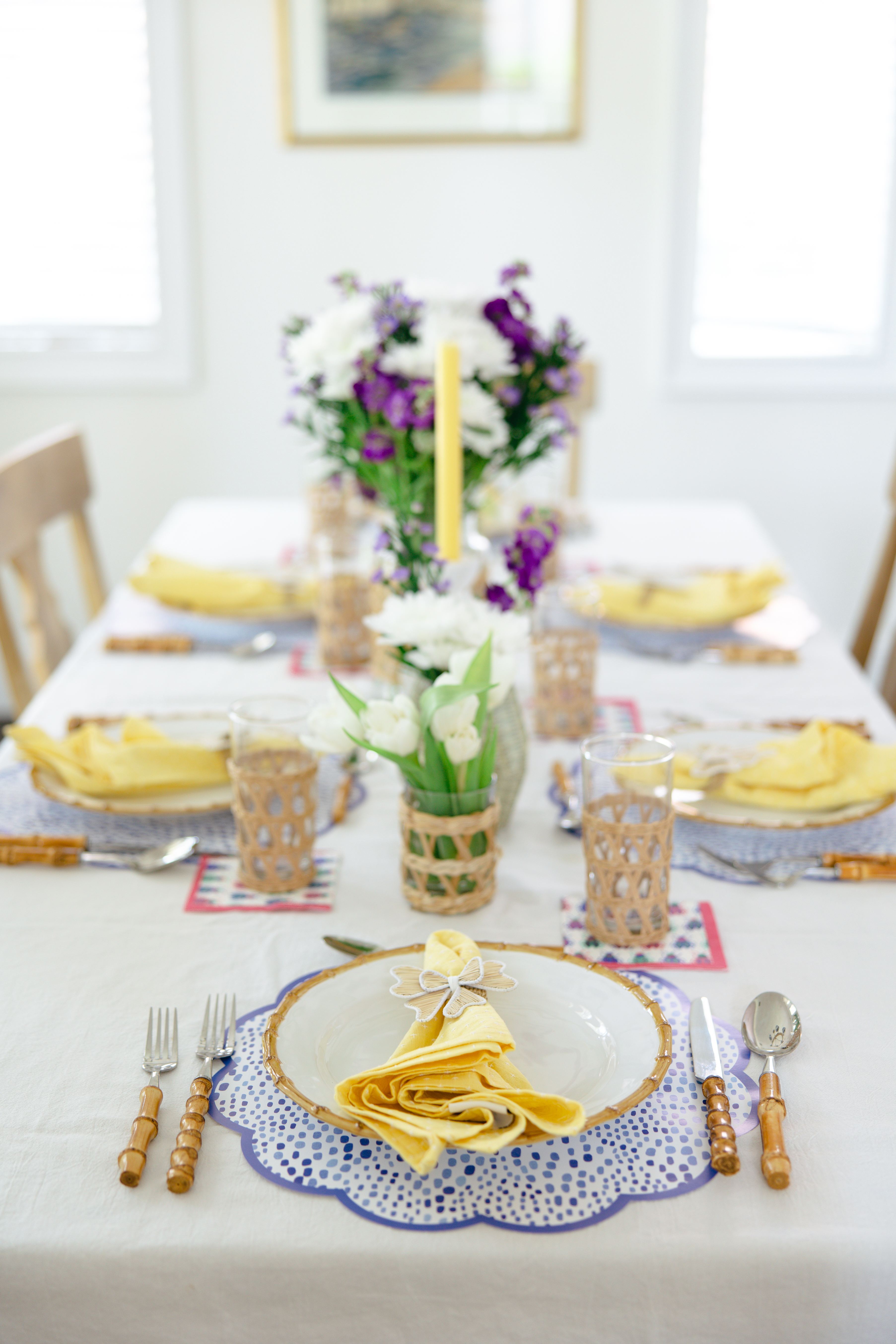 Table set with purple ikat placemats, bright yellow napkins and white and purple flowers as a centerpiece.