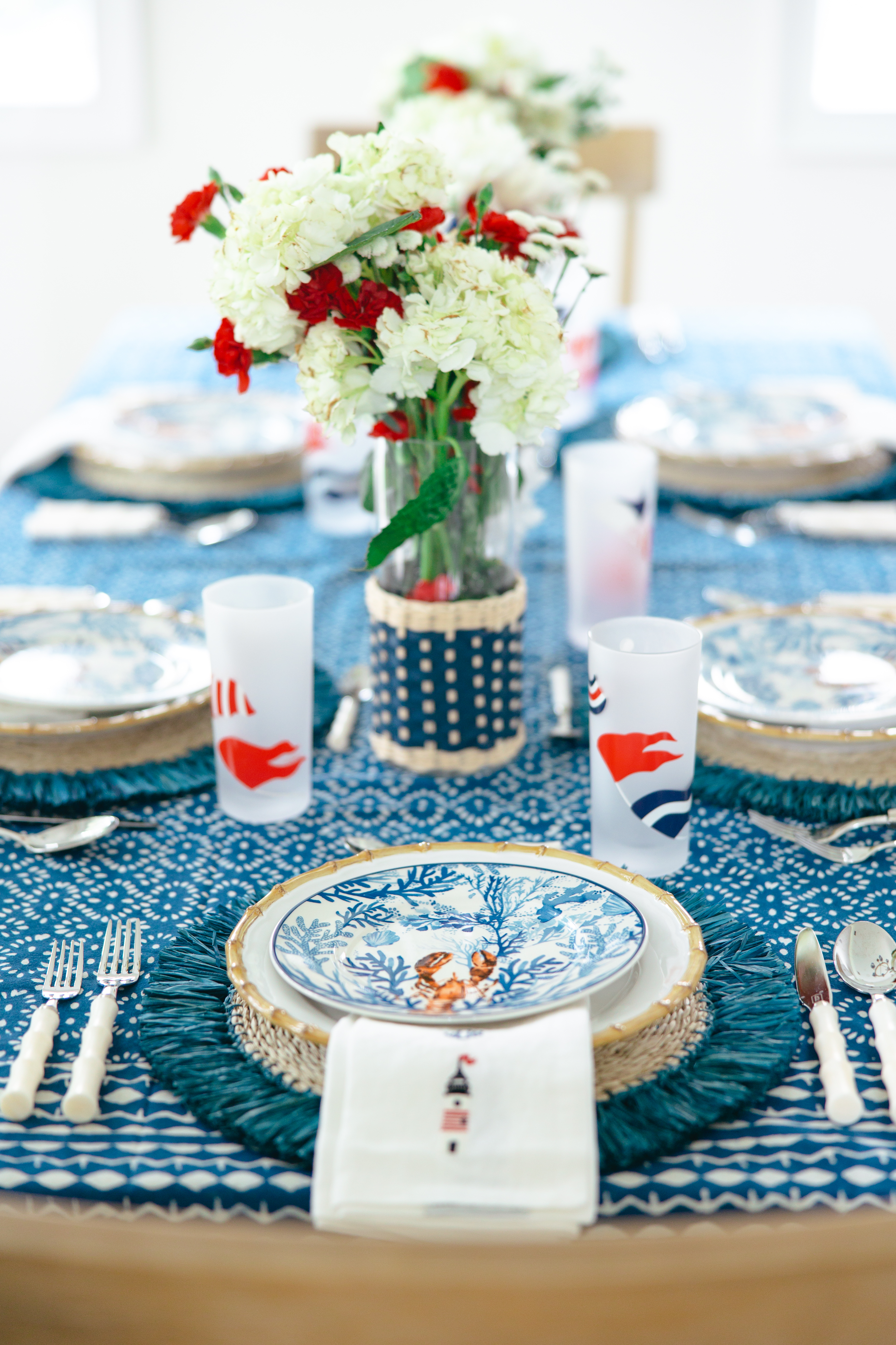 Fully set table with lobster plates, lighthouse napkins and nautical flag highball glasses.
