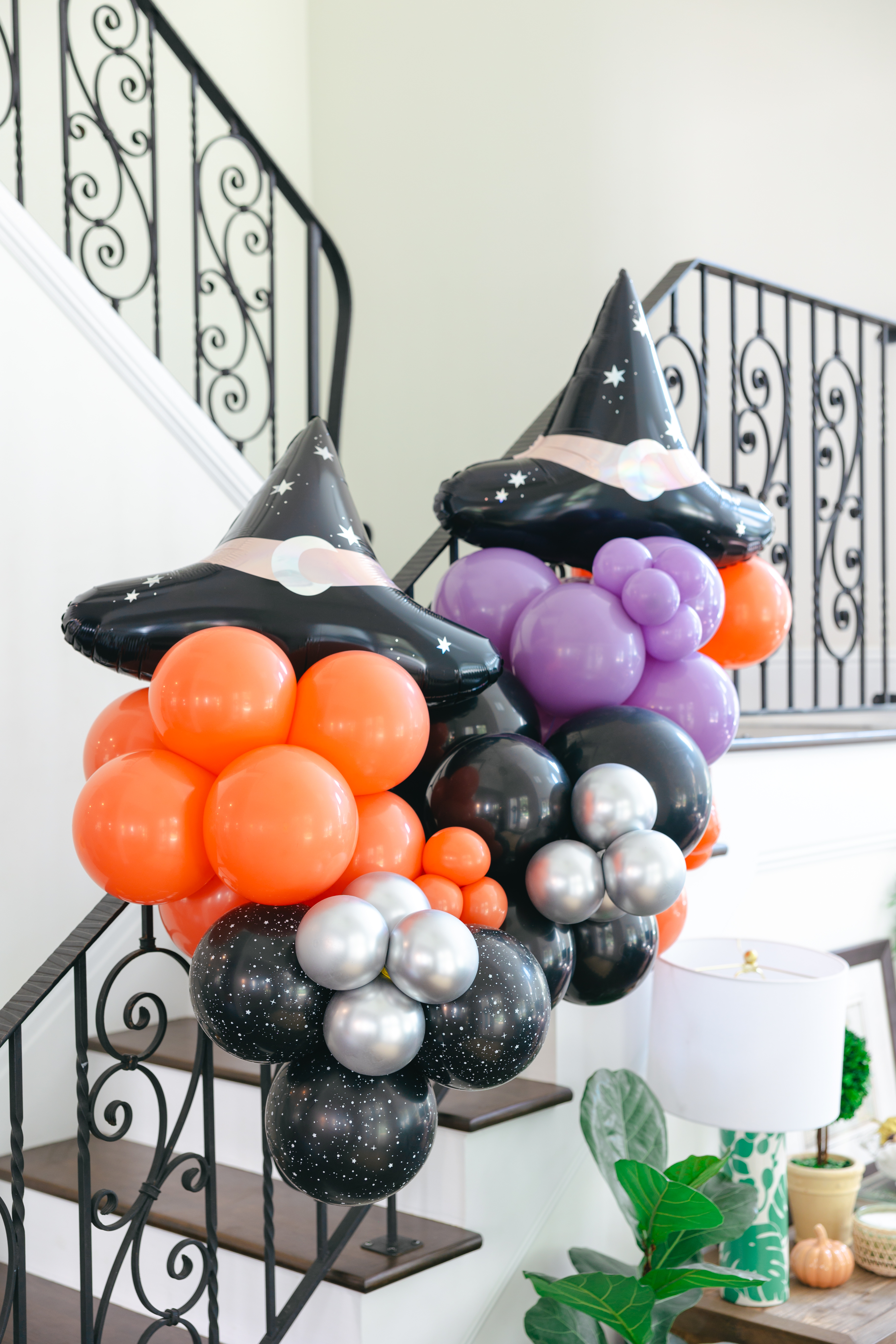 Small balloon arch on staircase with two witches hat foil balloons.